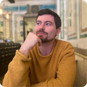 Image of Max Adams sitting in a cafe wearing a yellow jumper