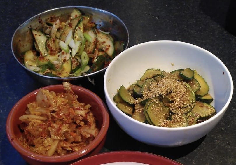 Three bowls containing different banchan: Oi-Muchim, Kimchi and Sesame Courgettes