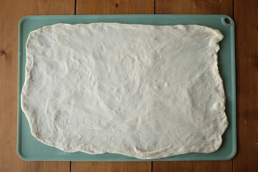 An image of dough stretched into a flat sheet on a green baking mat.