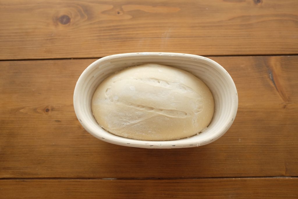 Dough that has been scored in a rectangle on top and left to prove in a proving basket.