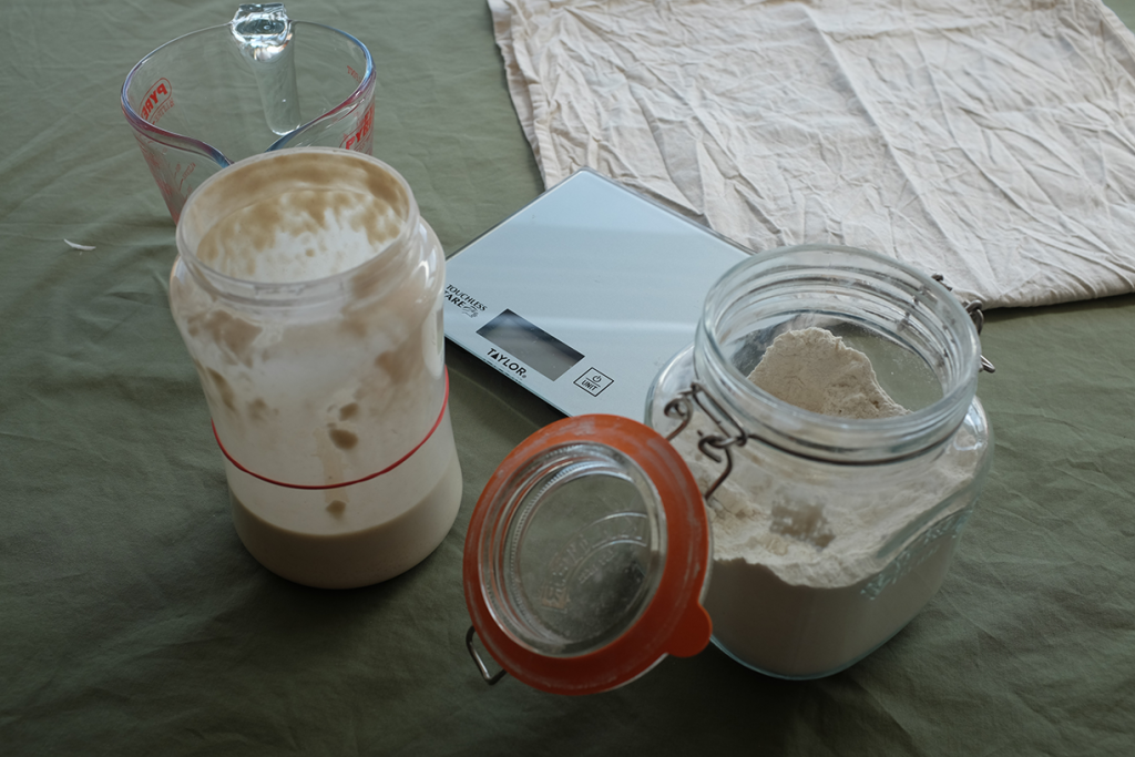 An image of the things you need to make a sourdough starter: a jug, starter jar, scales and flour