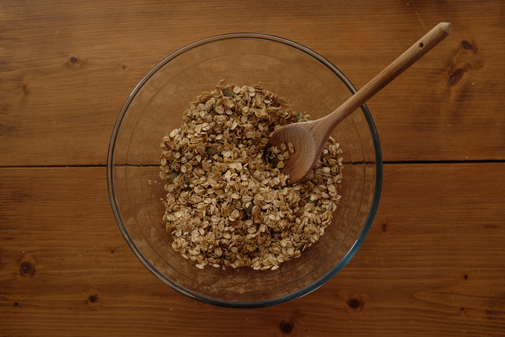 An overhead photo of a mixing bowl with oats and nuts mixed together with a wooden spoon.