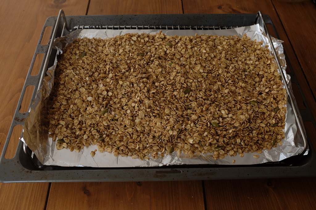 An image of oats and nuts spread flat on a baking tray lined with tin foil.