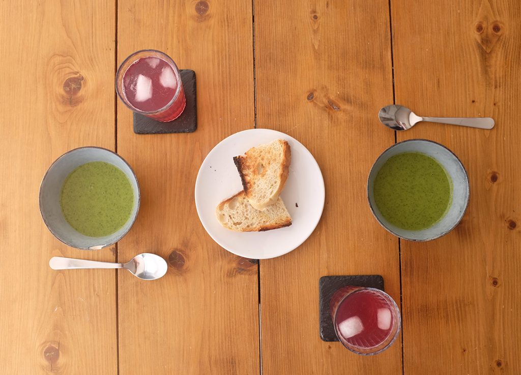 A photograph from above of two bowls of soup, a plate with two slices of sourdough bread and two glasses of home-made squash with ice.