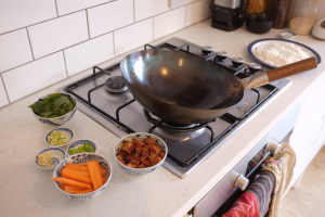 Image of a wok on a stove with the ingredients of pork fried rice in different bowls ready to be cooked