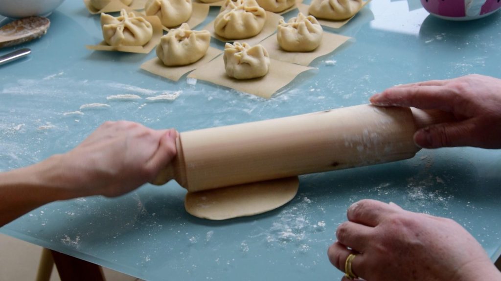 An image of two people using one hand each to roll a rolling pin over dough.