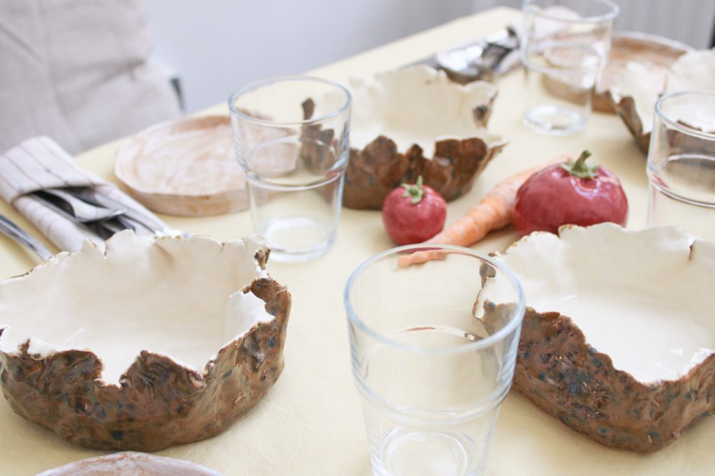 A table set for lunch, complete with hand-made ceramic vegetables and bowls designed to look like potato skins. 