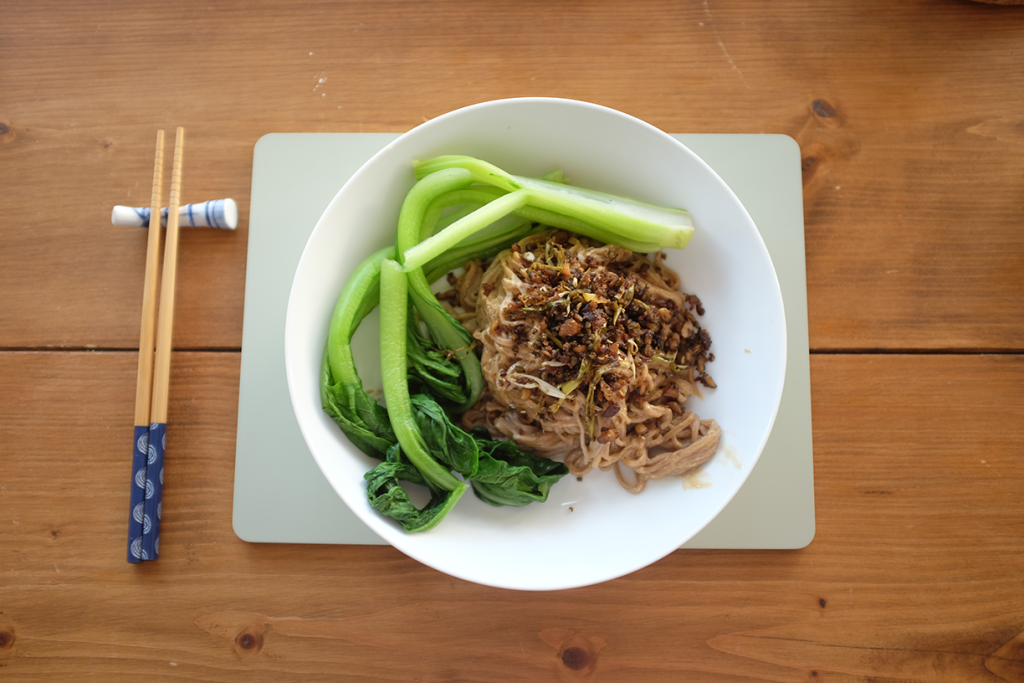 Image of a bowl of noodles and choi sum with some chopsticks.