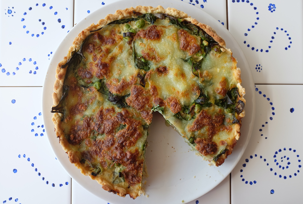 An overhead picture of a pea and leek tart with a slice missing.