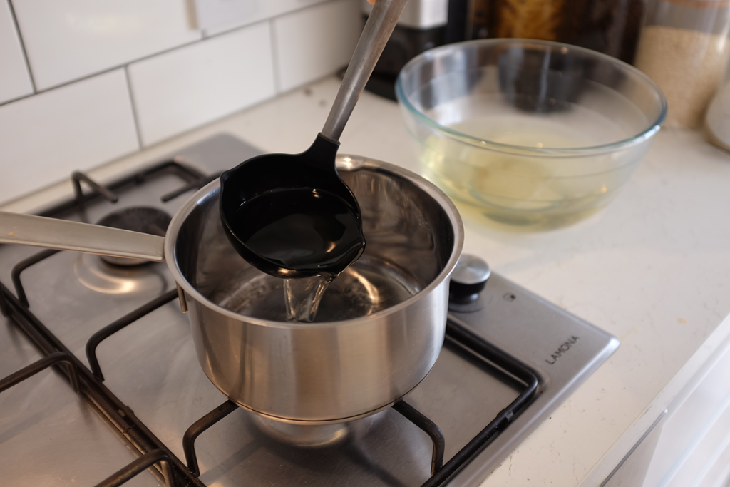 Adding dashi into a saucepan using a ladle.