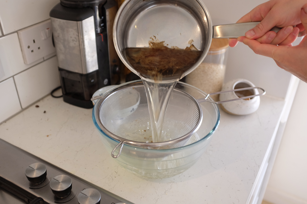 Straining katsuobushi flakes out of dashi with a sieve.