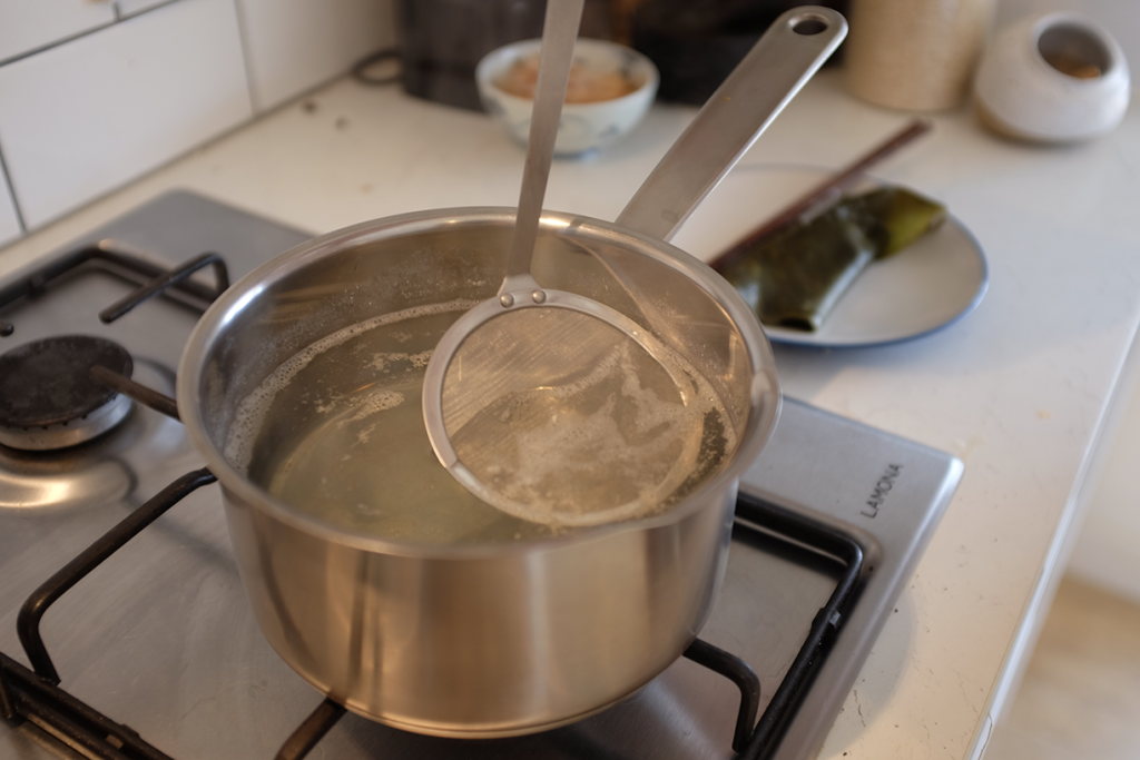 Skimming foam off the top of dashi with a skimmer.