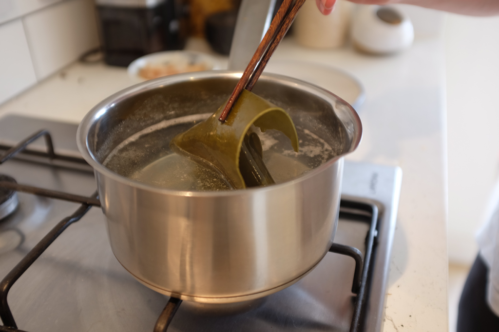 Lifting kombu out of hot water with chopsticks.