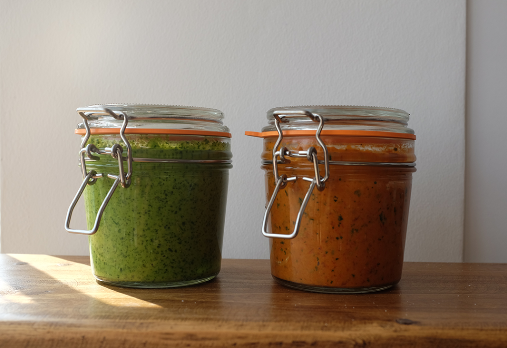 A jar of green pesto next to a jar of red pesto