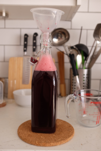 A bottle being filled with squash through a funnel.