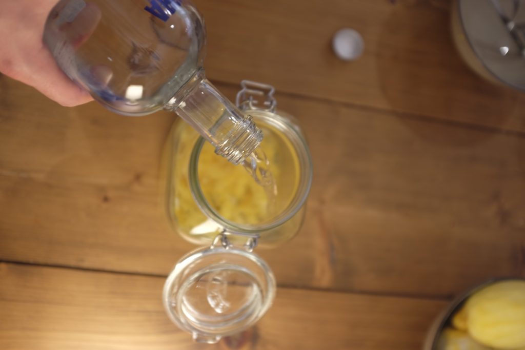 Vodka being poured into a Kilner jar with lemon zest in it.