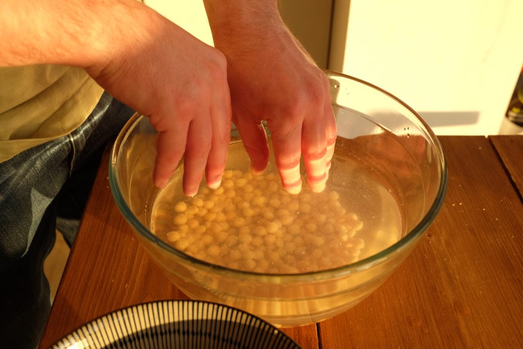 A man using his hands to peel shells off chickpeas in a bowl.